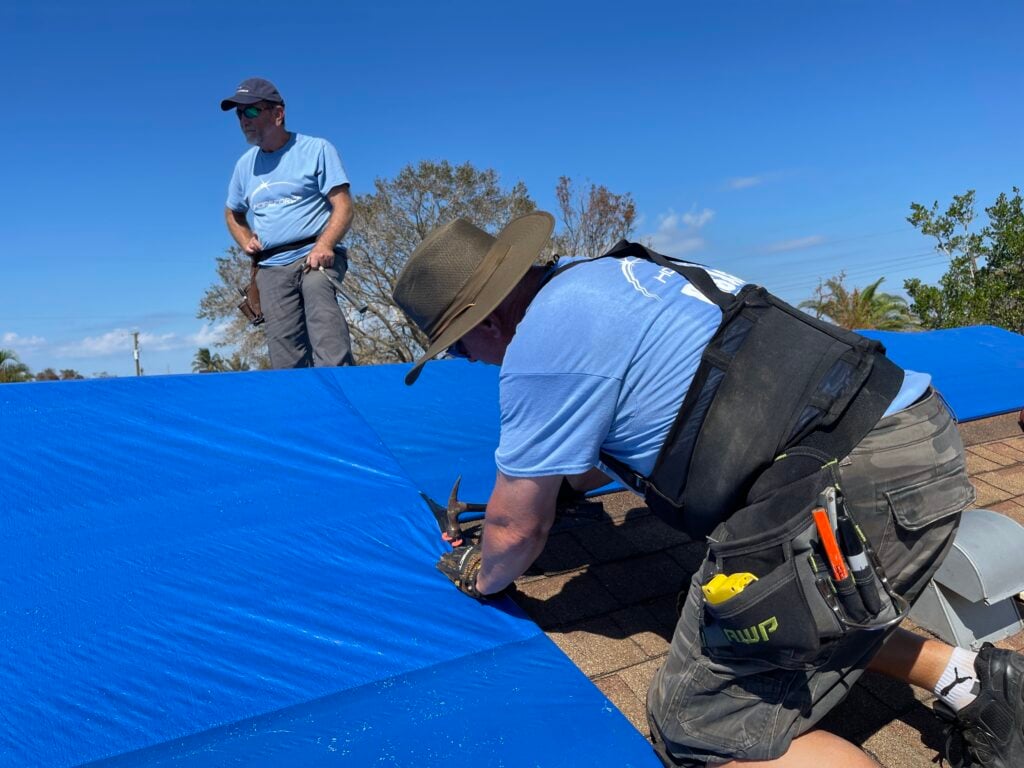 A Hope Force Reservist works to nail a tarp to a damaged roof.