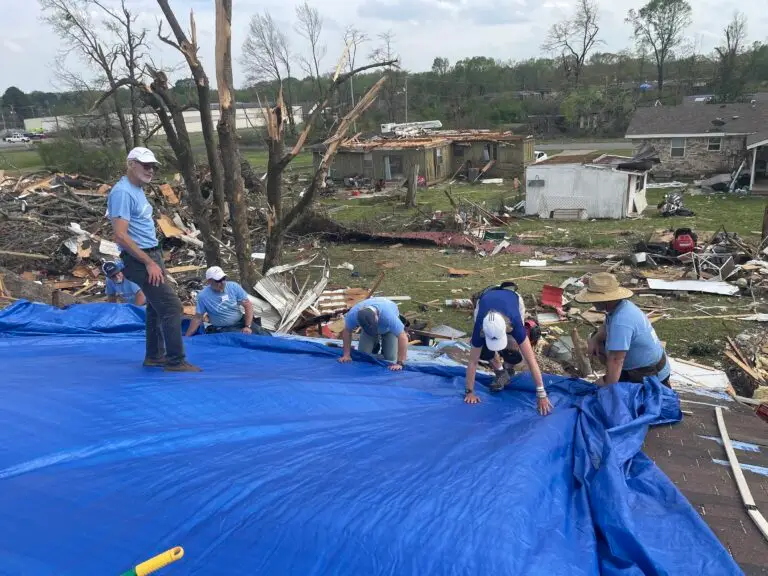 Hope Force Reservists secure a blue tarp to a roof in an area of severe tornado damage in Arkansas.