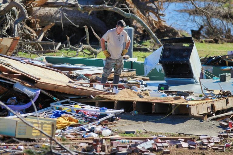 A disaster survivor stands among house rubble left by a tornado.